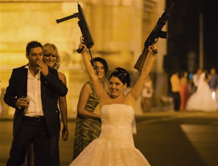 A Romanian bride holds toy weapons in the air at the Triumph Arch in Bucharest, Romania. The arch, a replica of the Arc de Triomphe in Paris,  is a rendezvous place for brides on the wedding night for the bride stealing ritual. 